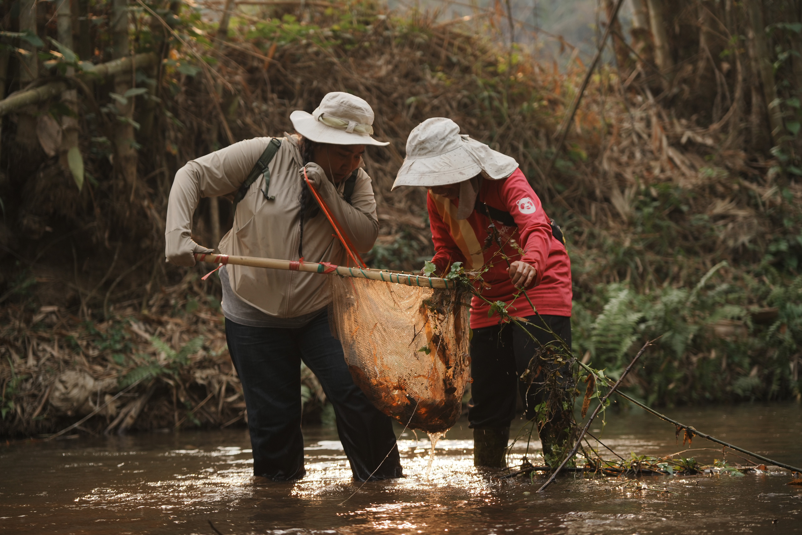 Chamonpat Khunwat, left, and her friend catching pla rak kluay with a traditional method during a biodiversity monitoring activity.